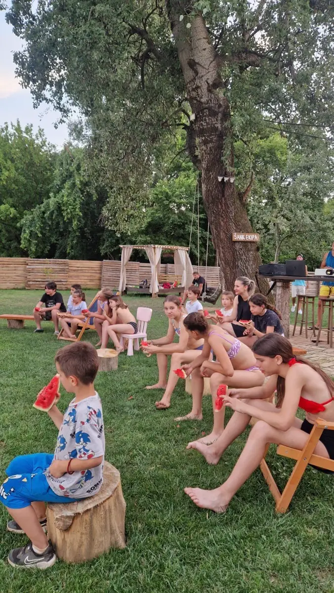 Deca jedu lubenicu na klupama pored reke leti